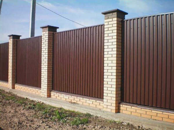 Профнастил в сочетании с кирпичными столбами выглядит солидно